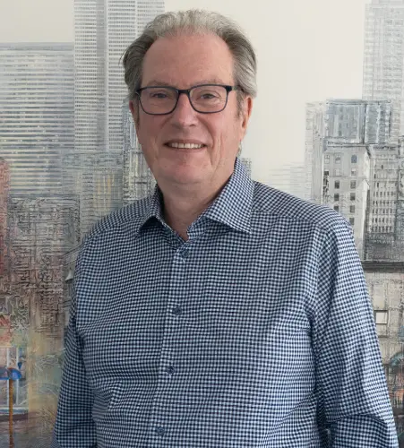 A man in glasses and a blue shirt standing next to a wall.