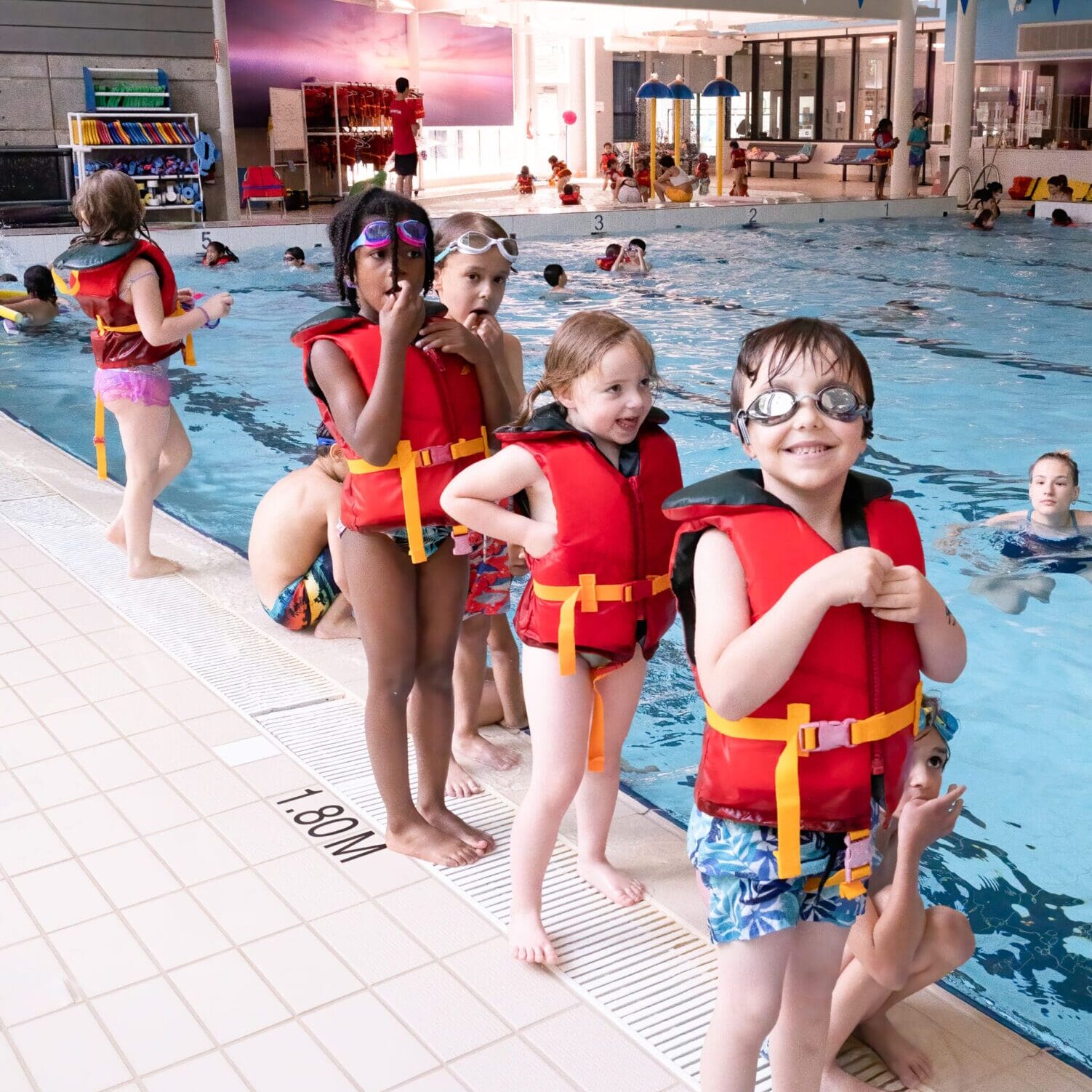 A group of children in the pool wearing life jackets.